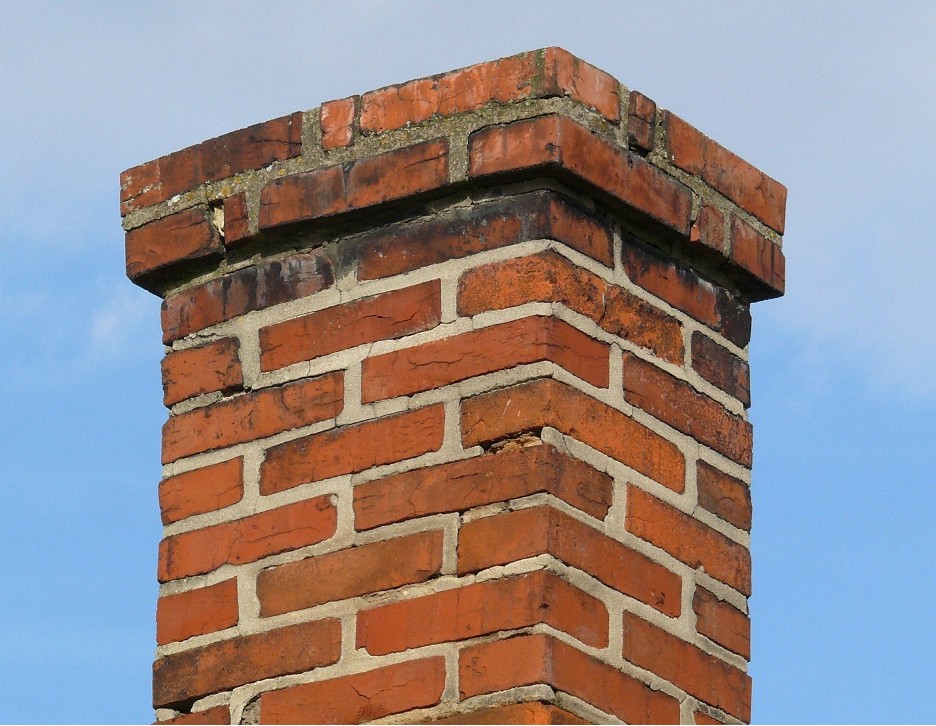 A slightly damaged and discolored brick chimney